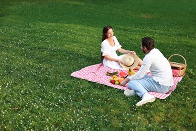 Happy couple having picnic on green grass outdoors. Space for text