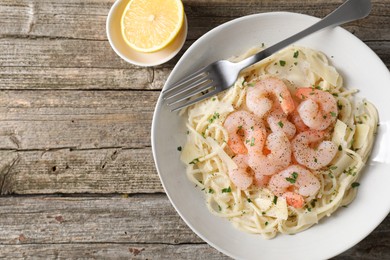 Photo of Delicious pasta with shrimps, cheese and lemon on wooden table, top view. Space for text