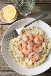 Photo of Delicious pasta with shrimps, cheese, lemon and water on wooden table, top view