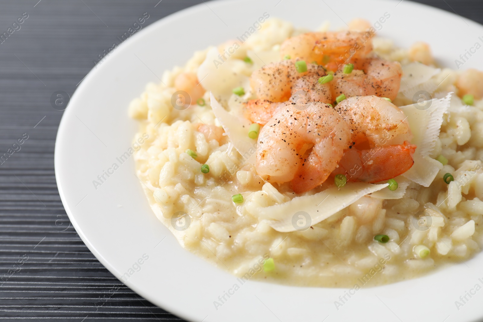 Photo of Delicious risotto with shrimps and cheese on black table, closeup