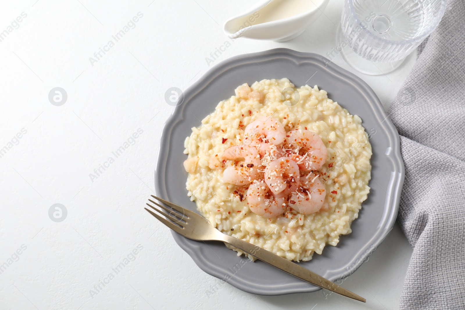 Photo of Delicious risotto with shrimps, cheese, sauce and water on white table, top view. Space for text