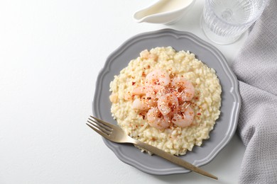 Photo of Delicious risotto with shrimps, cheese, sauce and water on white table, top view. Space for text