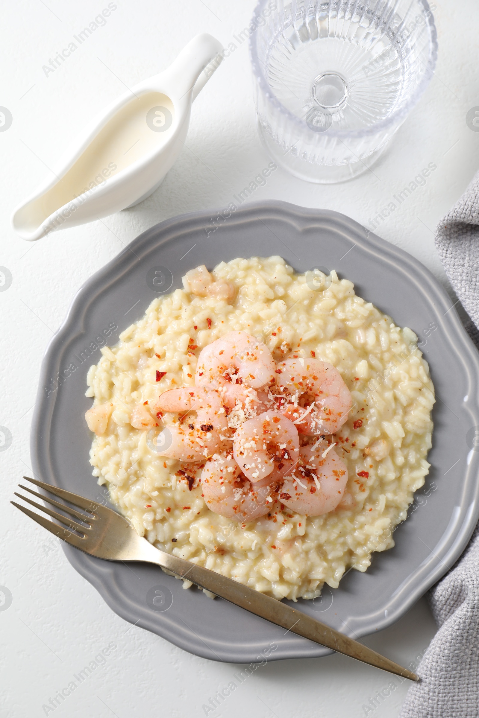 Photo of Delicious risotto with shrimps, cheese, sauce and water on white table, top view