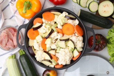 Cooking stew. Cut raw vegetables in pot and other ingredients on white table, flat lay