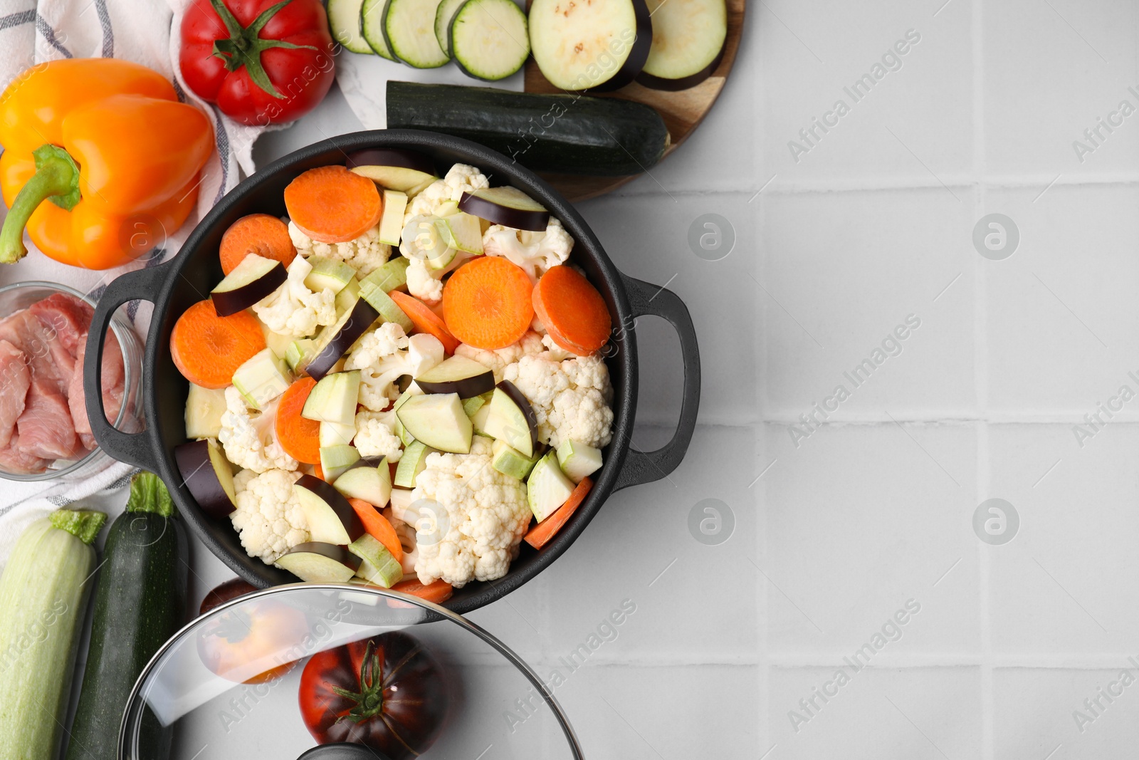 Photo of Cooking stew. Cut raw vegetables in pot and other ingredients on white tiled table, flat lay