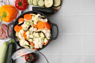 Cooking stew. Cut raw vegetables in pot and other ingredients on white tiled table, flat lay