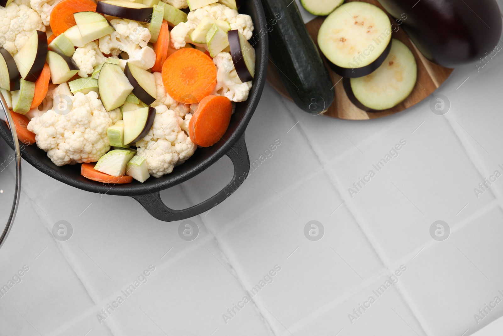 Photo of Cooking stew. Cut raw vegetables in pot on white tiled table, flat lay