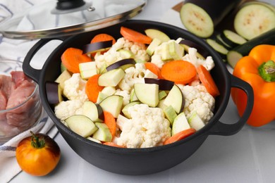 Cooking stew. Cut raw vegetables in pot and other ingredients on white tiled table, closeup