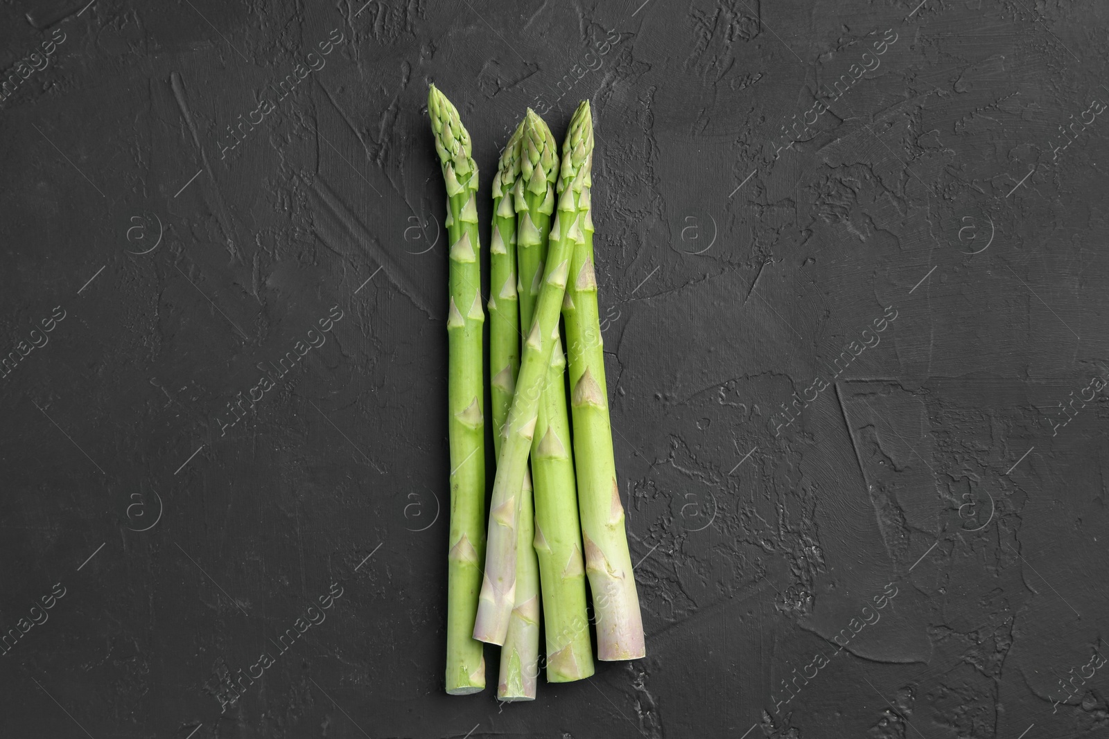 Photo of Fresh green asparagus stems on gray textured table, top view