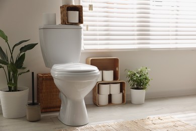 Photo of White toilet bowl, paper rolls and houseplants in bathroom