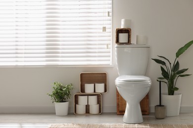 Photo of White toilet bowl, paper rolls and houseplants in bathroom