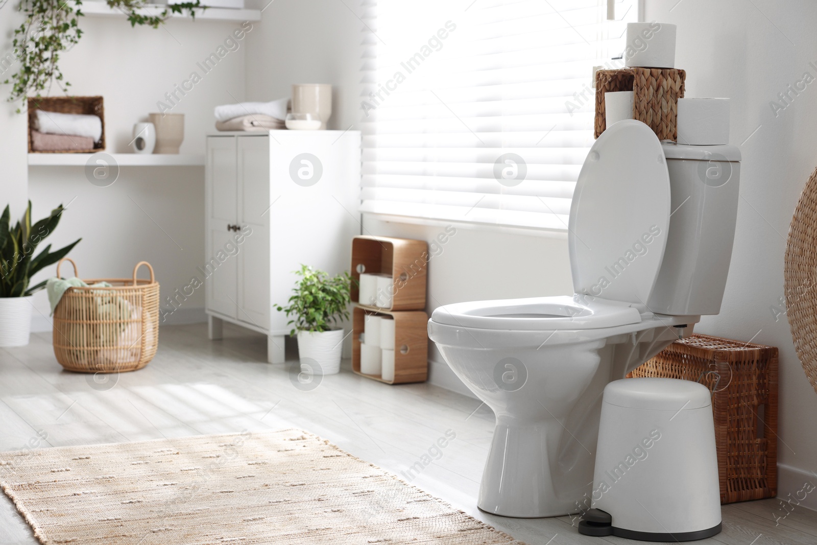 Photo of White toilet bowl, trash can and paper rolls in bathroom