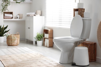 Photo of White toilet bowl, trash can and paper rolls in bathroom