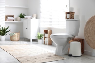 Photo of White toilet bowl, paper rolls and houseplants in bathroom