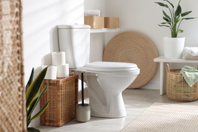 Photo of White toilet bowl, paper rolls and houseplants in bathroom