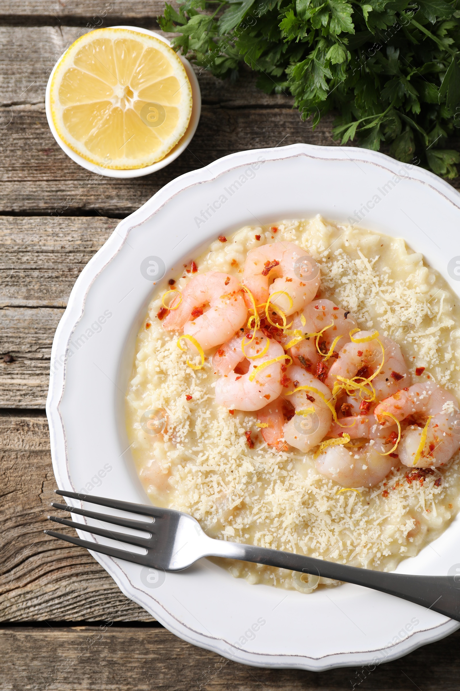 Photo of Delicious risotto with shrimps, cheese, lemon and parsley on wooden table, top view