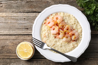 Photo of Delicious risotto with shrimps, cheese, lemon and parsley on wooden table, top view