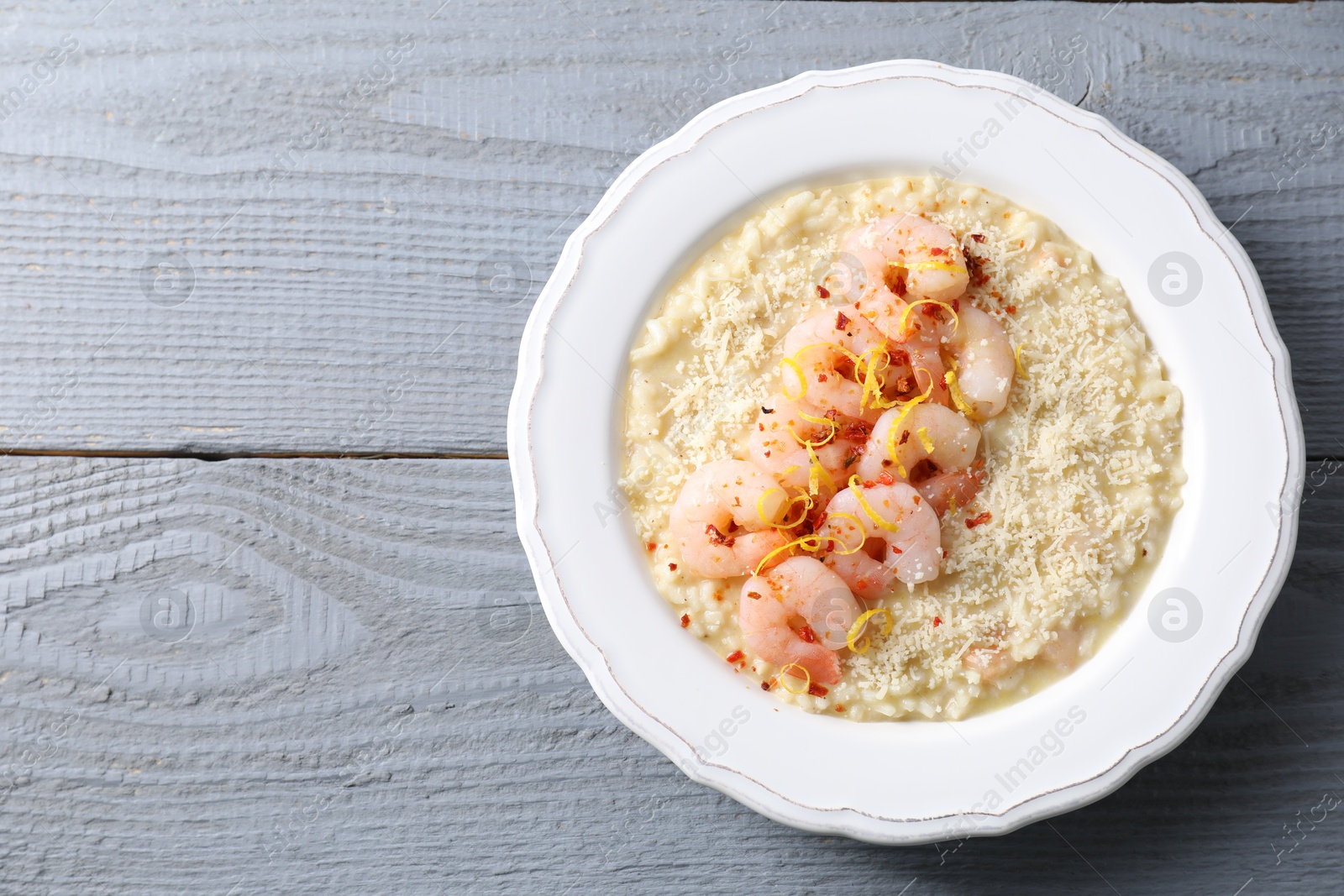 Photo of Delicious risotto with shrimps and cheese on grey wooden table, top view. Space for text