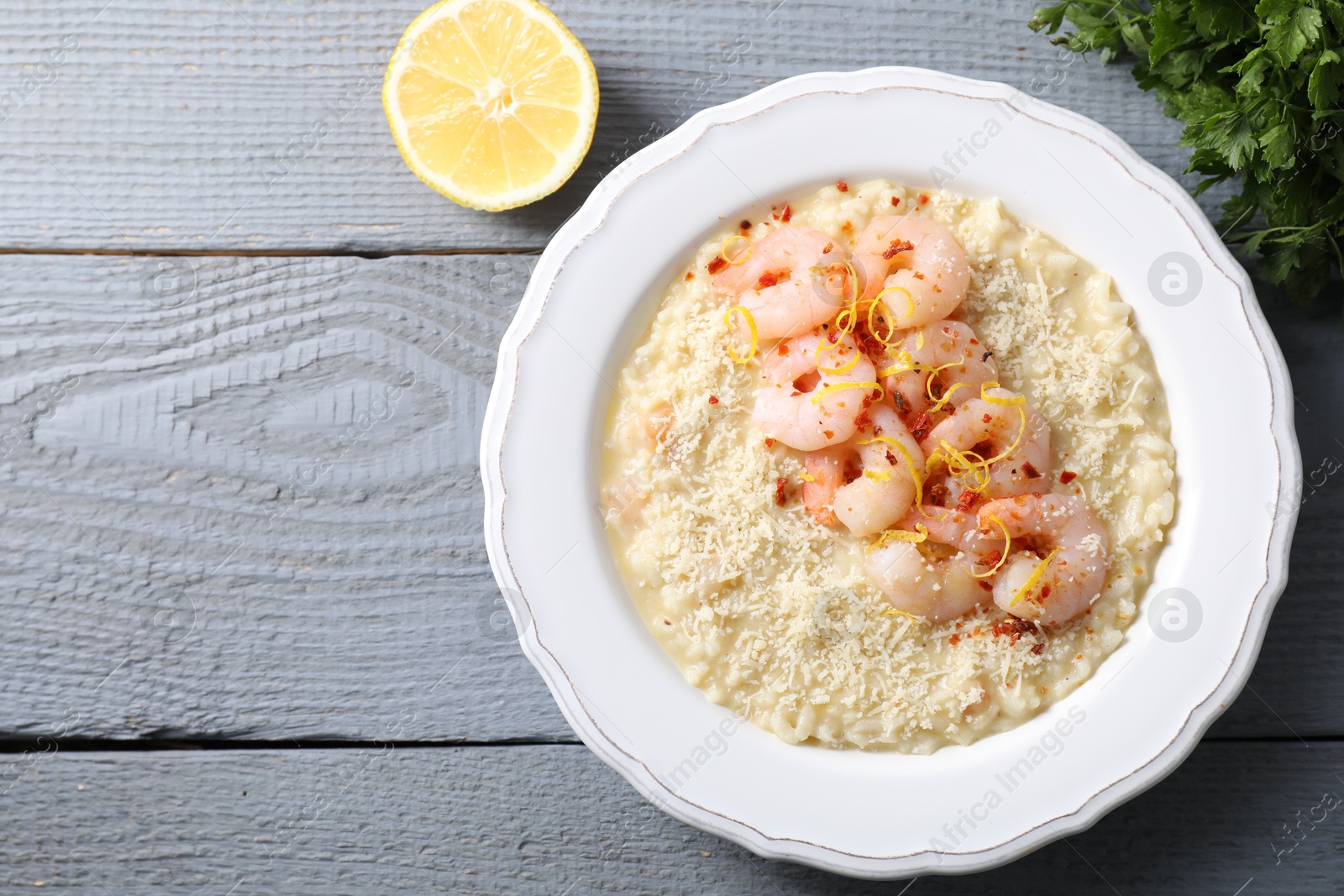 Photo of Delicious risotto with shrimps, cheese, lemon and parsley on grey wooden table, top view. Space for text