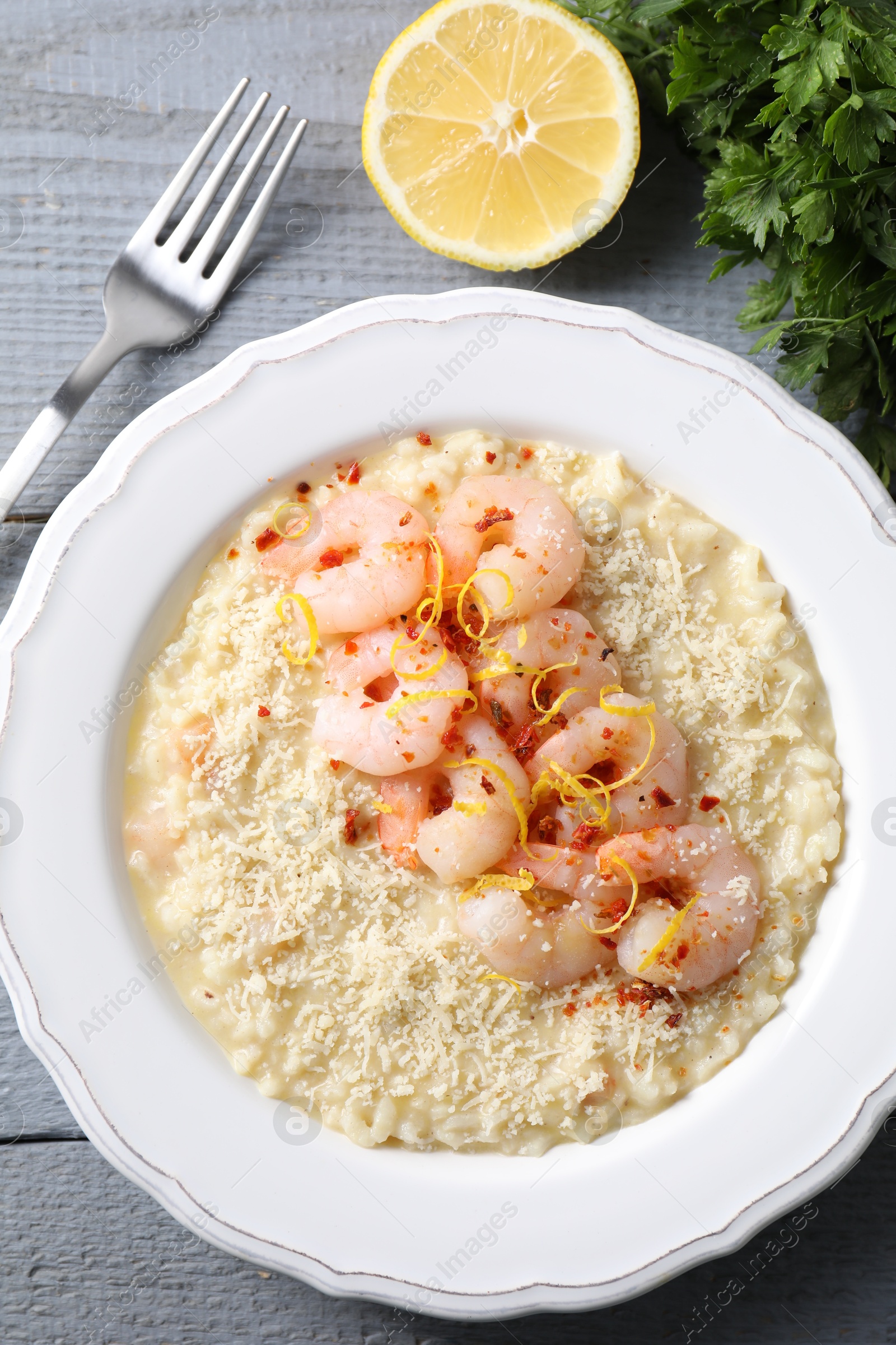 Photo of Delicious risotto with shrimps, cheese, lemon and parsley on grey wooden table, top view