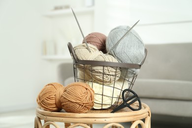 Photo of Skeins of soft yarn, knitting needles and scissors on table indoors