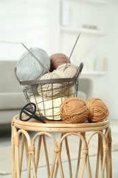 Photo of Skeins of soft yarn, knitting needles and scissors on table indoors