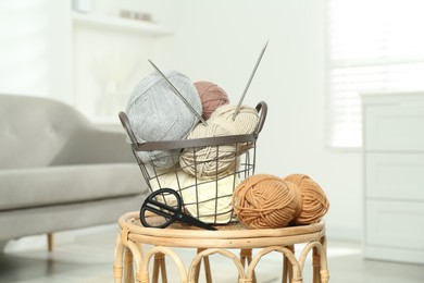 Photo of Skeins of soft yarn, knitting needles and scissors on table indoors