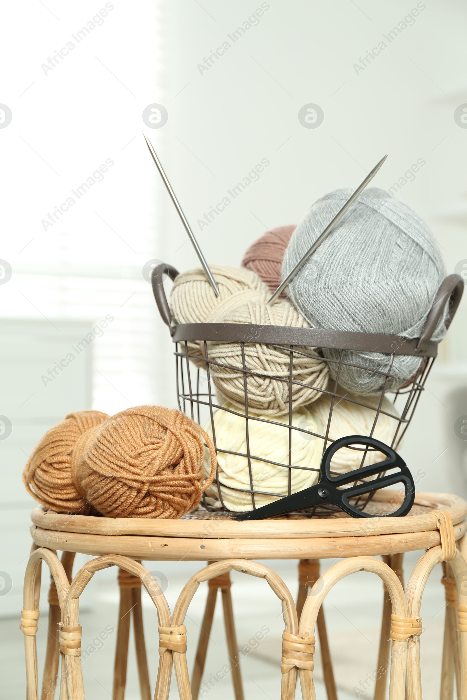 Photo of Skeins of soft yarn, knitting needles and scissors on table indoors