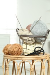 Photo of Skeins of soft yarn, knitting needles and scissors on table indoors