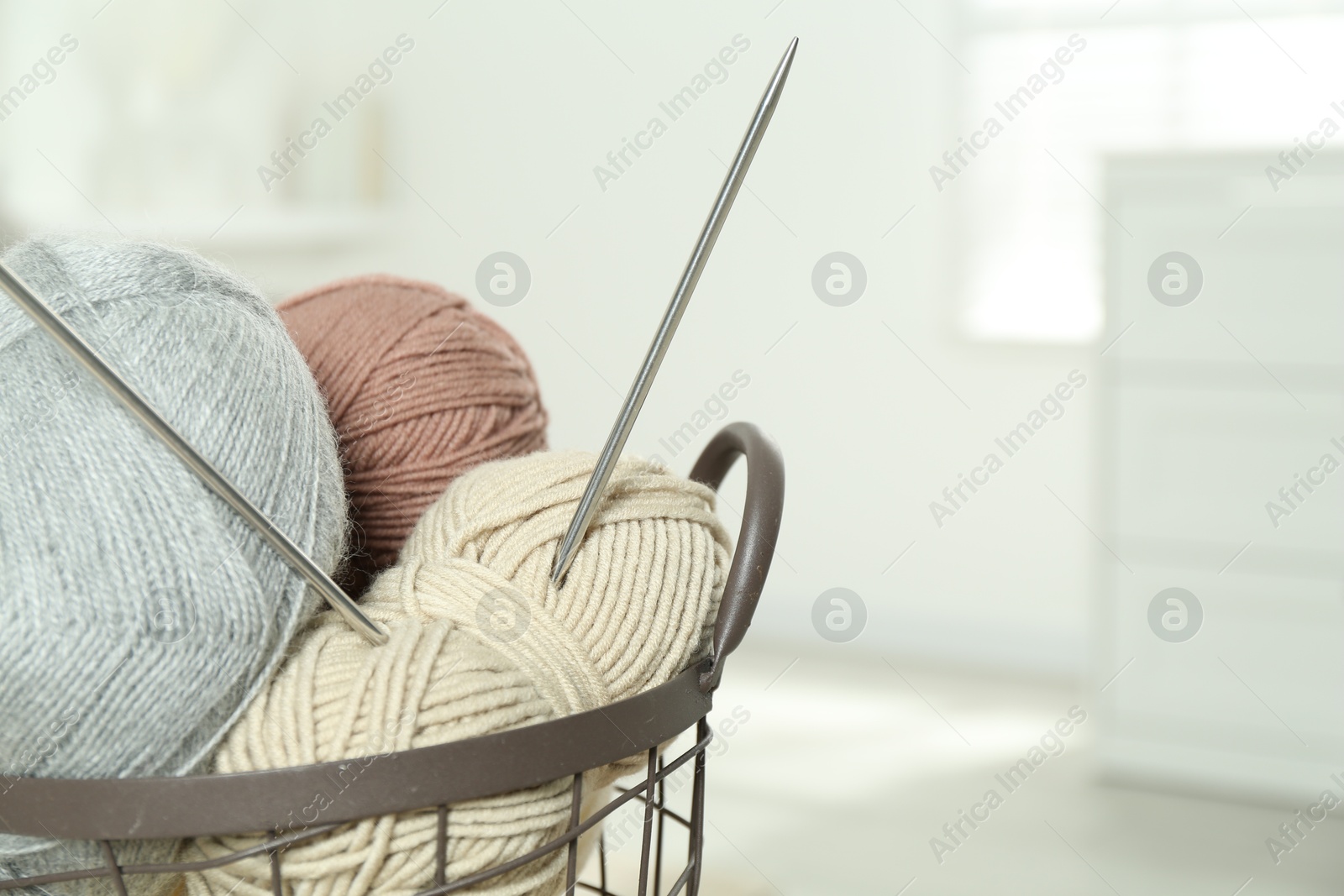 Photo of Skeins of soft yarn and knitting needles in basket indoors, closeup. Space for text