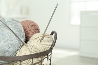 Photo of Skeins of soft yarn and knitting needles in basket indoors, closeup. Space for text