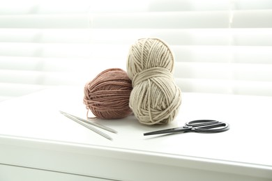 Soft yarn, knitting needles and scissors on chest of drawers indoors