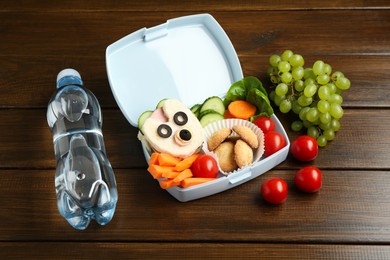 Photo of Lunch box with sandwich, fresh vegetables, cookies, grapes and bottle of water on wooden table