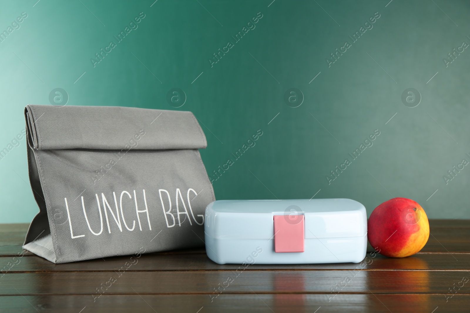 Photo of Gray bag, lunch box and fresh peach on wooden table against color background