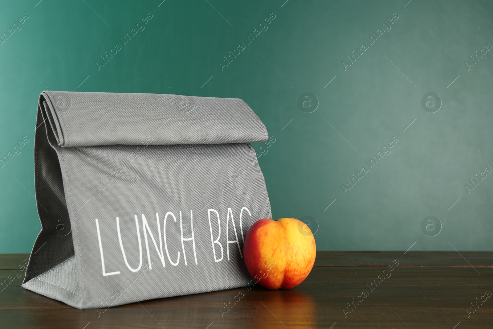 Photo of Lunch bag and fresh peach on wooden table against color background, space for text