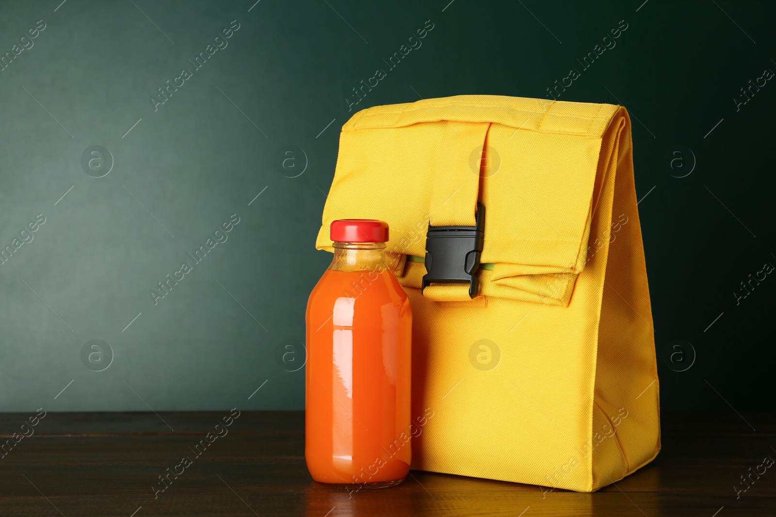 Photo of Lunch bag and bottle of juice on wooden table against color background, space for text