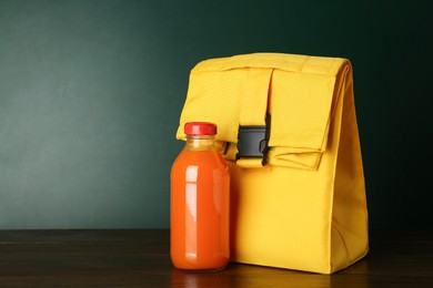 Photo of Lunch bag and bottle of juice on wooden table against color background, space for text