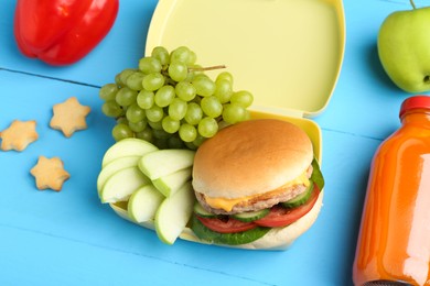 Photo of Plastic lunch box with burger, fresh fruits, bottle of juice, bell pepper and cookies on light blue wooden table, above view