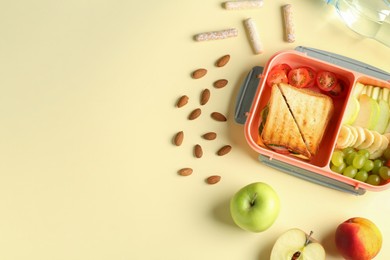 Photo of Lunch box with snacks and bottle of water on yellow table, flat lay. Space for text