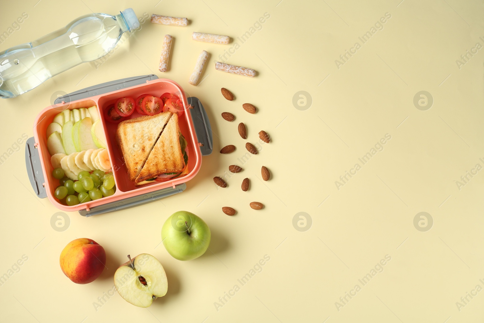 Photo of Lunch box with snacks and bottle of water on yellow table, flat lay. Space for text