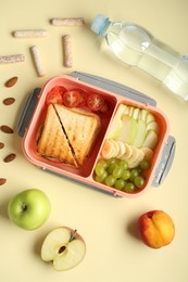 Photo of Lunch box with snacks and bottle of water on yellow table, flat lay