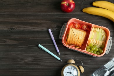 Photo of Lunch box with snacks, bottle of water, alarm clock and pens on wooden table, flat lay. Space for text