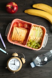 Photo of Lunch box with snacks, bottle of water, alarm clock and pens on wooden table, flat lay