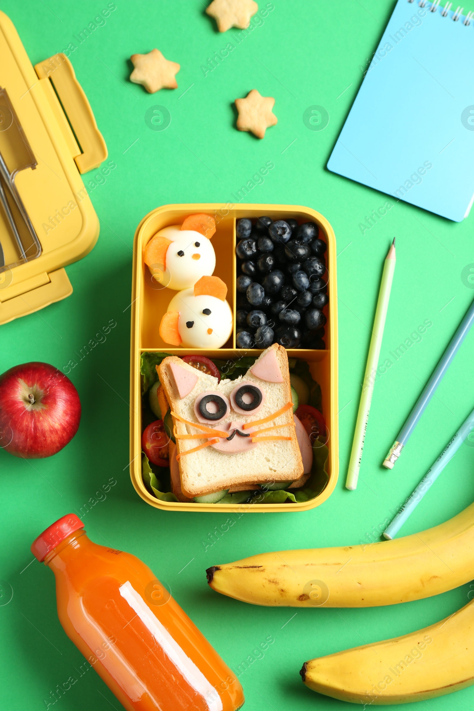 Photo of Lunch box with snacks, bottle of juice and stationery on green table, flat lay