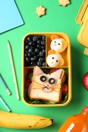 Photo of Lunch box with snacks, bottle of juice and stationery on green table, flat lay