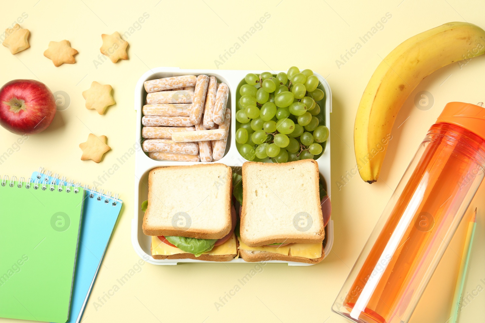 Photo of Lunch box with snacks, bottle and stationery on yellow table, flat lay