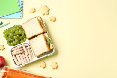 Photo of Lunch box with snacks, bottle and stationery on yellow table, flat lay. Space for text