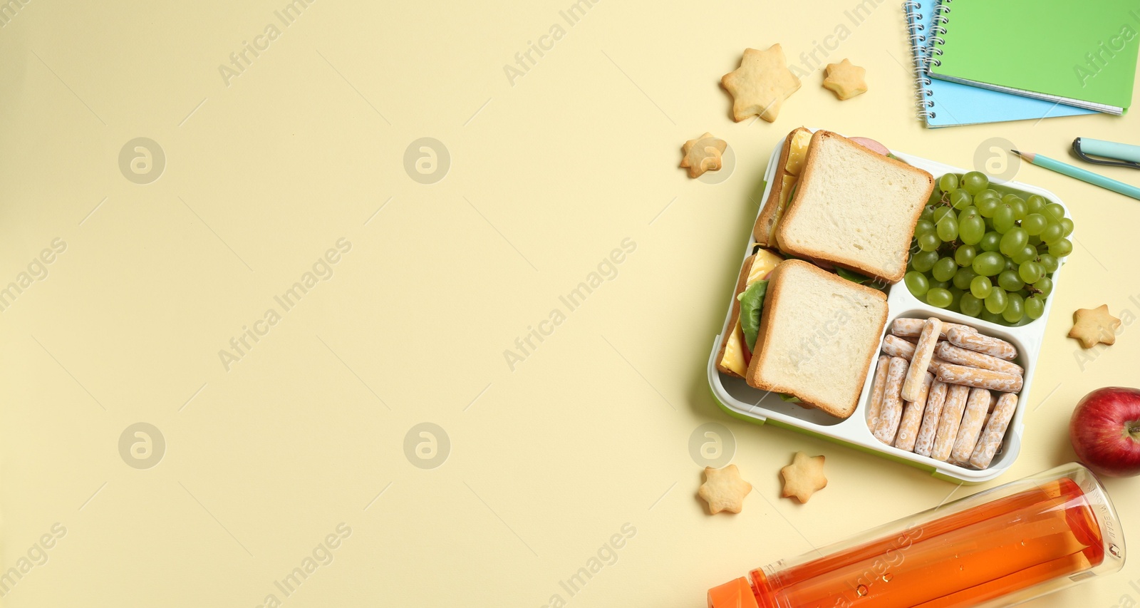 Photo of Lunch box with snacks, bottle and stationery on yellow table, flat lay. Space for text