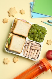 Photo of Lunch box with snacks, bottle and stationery on yellow table, flat lay