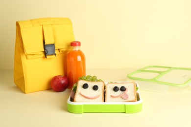 Photo of Bag, sandwiches with smiley faces in lunch box and bottle of juice a on yellow background